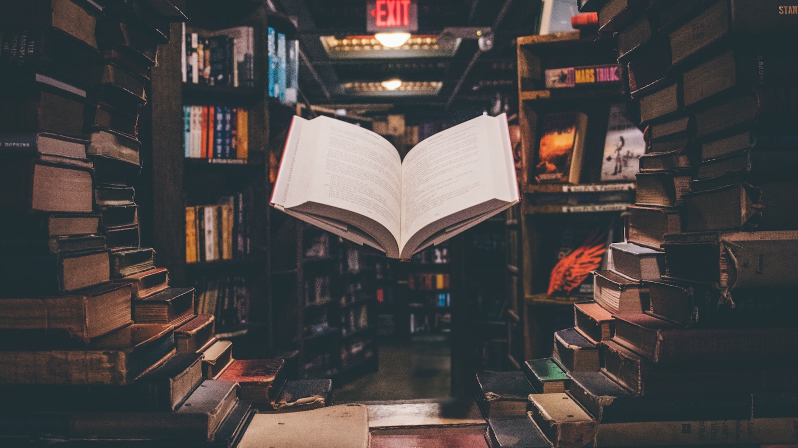 Student writing notes by hand at a desk surrounded by open books