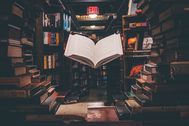 Student writing notes by hand at a desk surrounded by open books